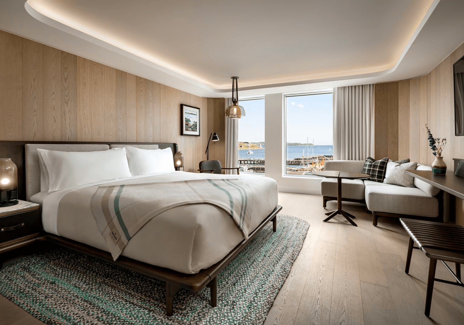 Guest room at Muir Halifax, designed by Studio Munge, featuring a custom tartan blanket created by Love & War as part of the hotel's visual identity. Inspired by Nova Scotia's maritime landscape and color palette, the bespoke textile extends the brand into the guest experience through locally rooted design and craftsmanship.