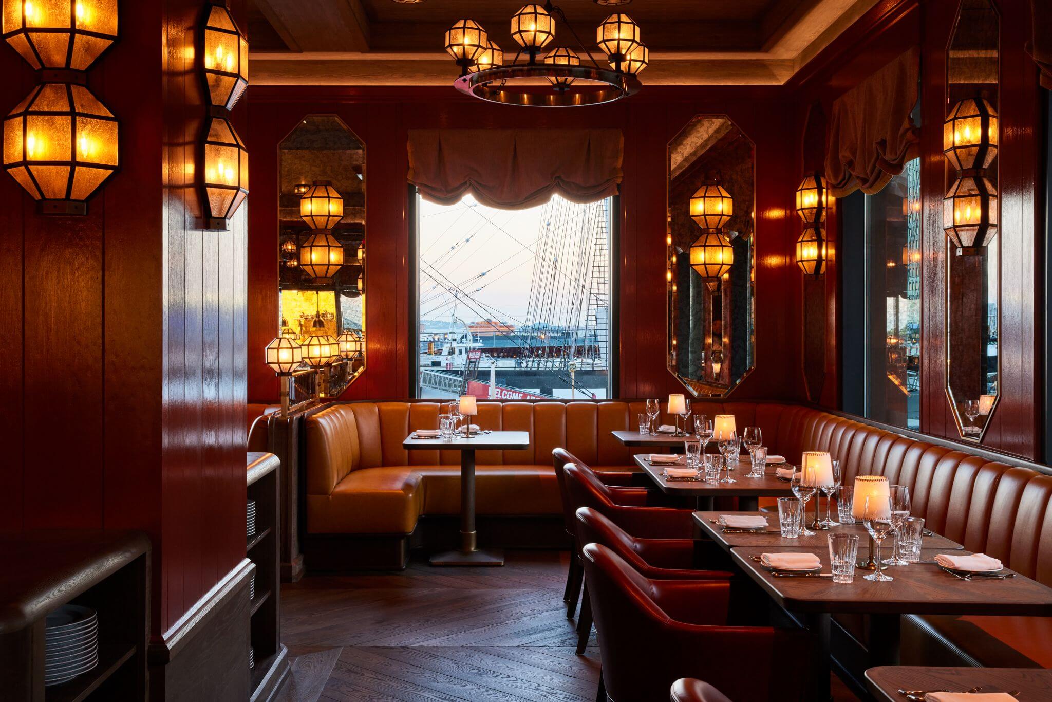 Carne Mare dining room at Pier 17 overlooking the South Street Seaport, with rich red interiors, leather banquettes and waterfront views.