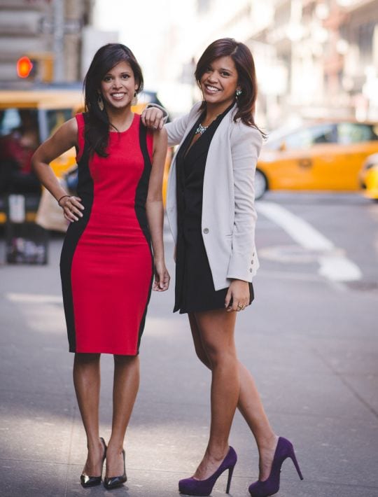 Two women wearing high heels posing on a street corner with a busy street in the background