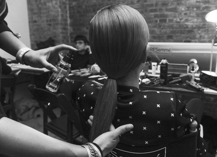 A stylist tying two sections of a model's hair together at the back of her head