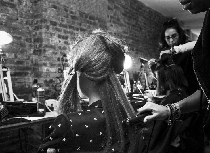 A model with a parting and a stylist about to apply some product to her hair with a comb