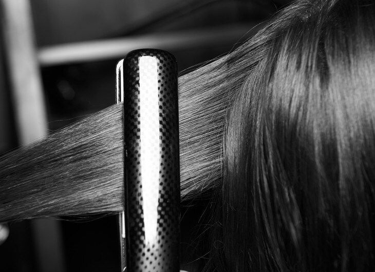 The back of a model's head with a section of her long dark hair in hot irons