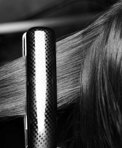 The back of a model's head with a section of her long dark hair in hot irons
