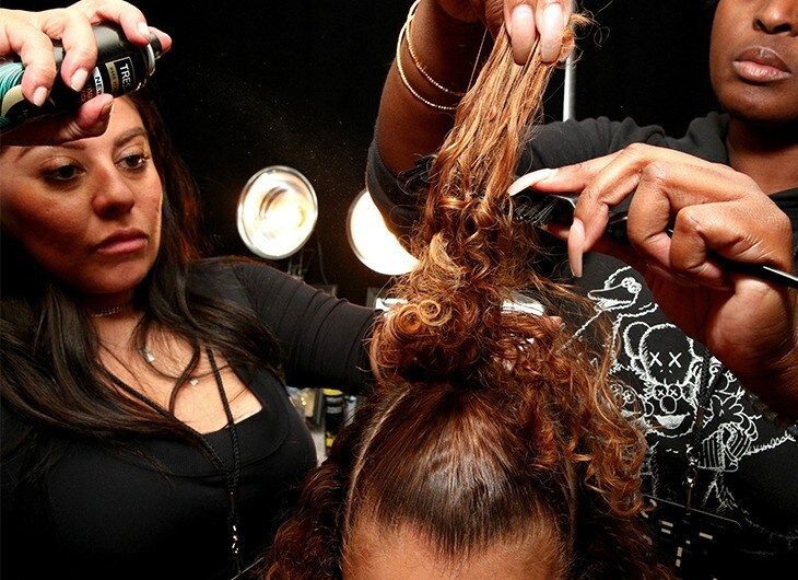 Two stylist's teasing and spraying a model's mini ponytail.