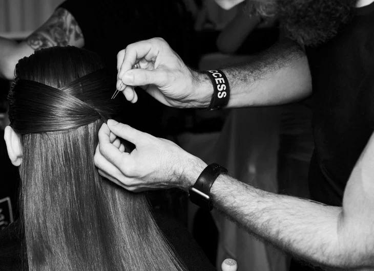 A stylist's hands tying sections of a model's hair together with the help of a bobby pin