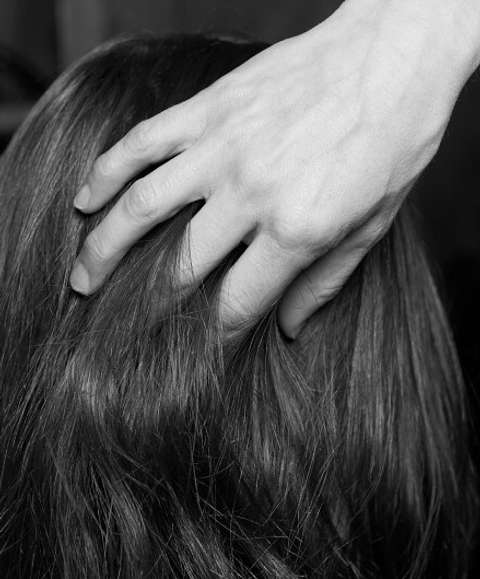 A close up of the back of a model's head with a stylist's hand running through it
