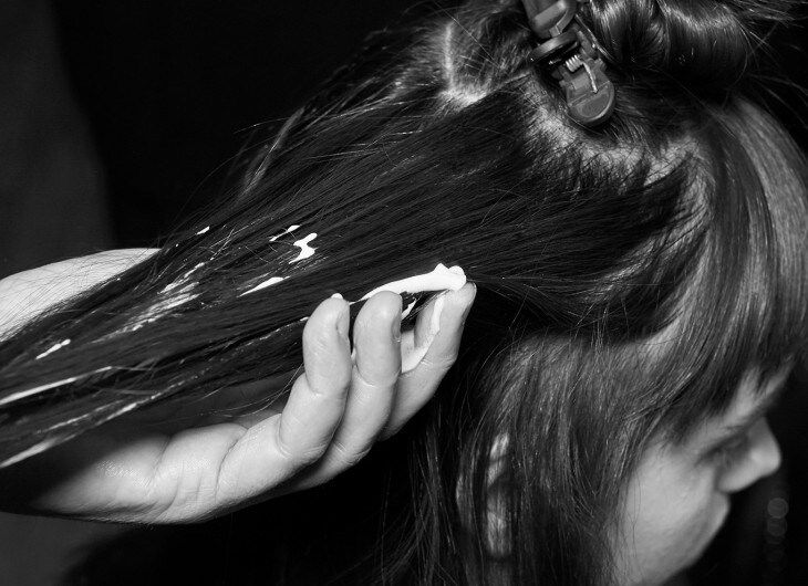 A model with her hair in a clip and a stylist's hands appling mousse to a section of it