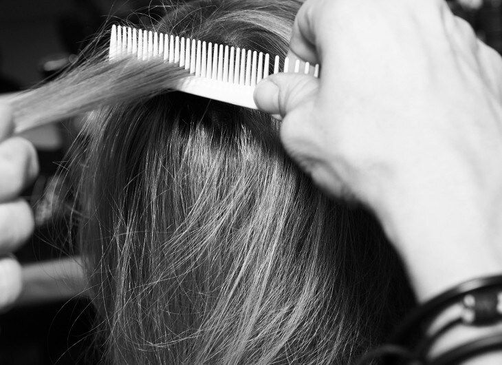 The back of a model's head and the hands of a stylist using a comb on a section of the hair