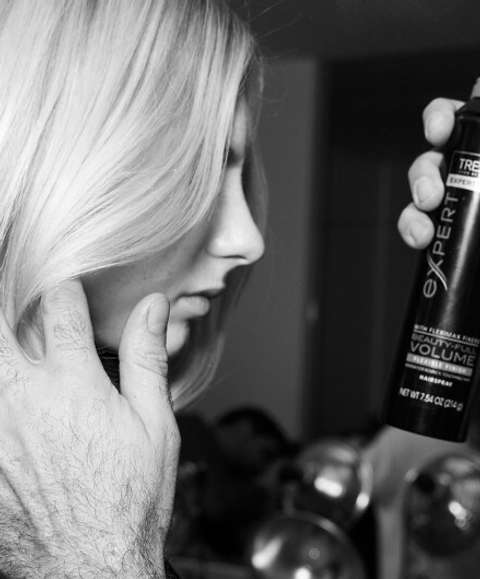 A stylist applying hairspray to a blonde model's hair