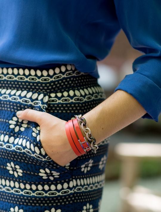 Closeup shot of a woman wearing a blue top, and bracelets on her arm, standing with her hand in her pocket