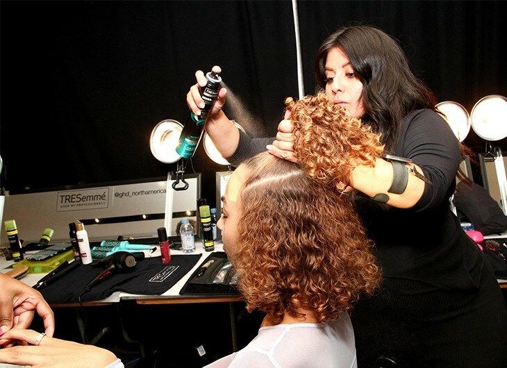 Woman teasing out a model's curly brown hair.