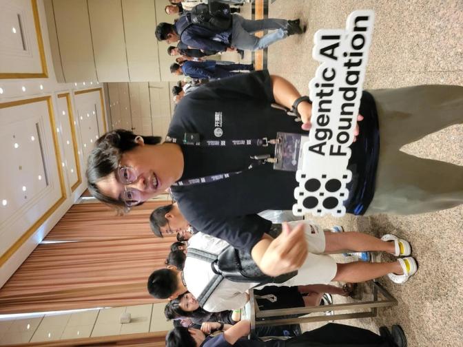 Attendee holding an Agentic AI Foundation sign at a tech conference with other participants in the background