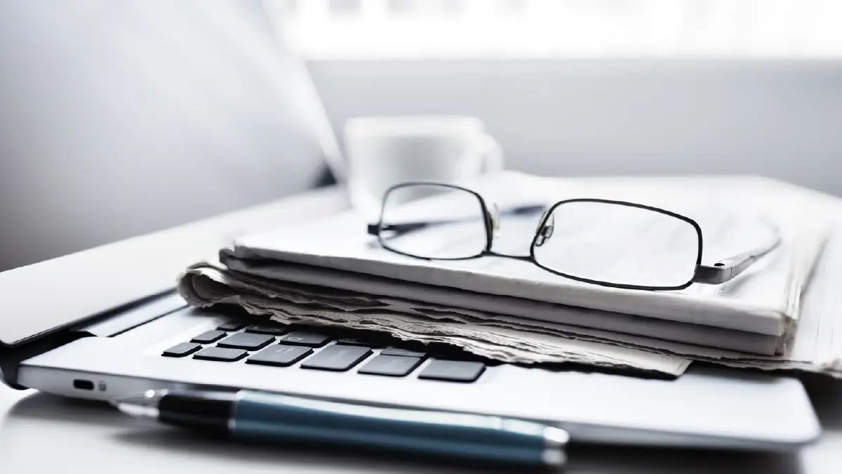Periódico doblado junto a lentes y un lápiz sobre el teclado de un computador portátil, representando la revisión de distintas fuentes de información antes de decidir dónde comprar una propiedad