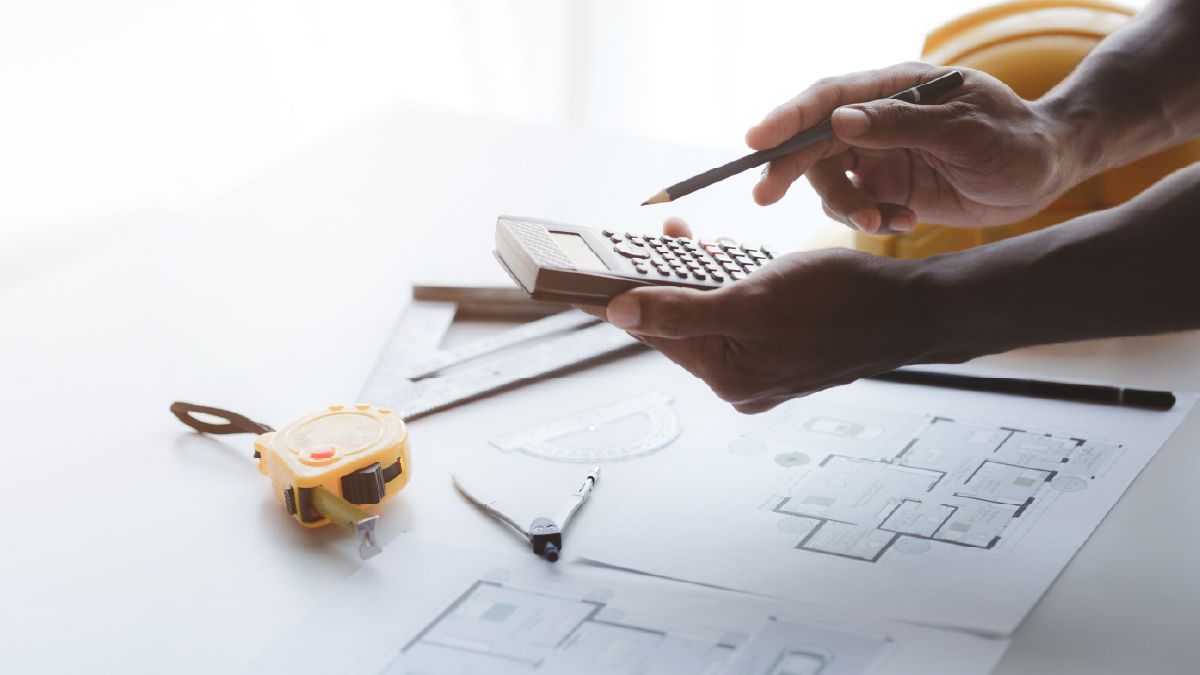 Persona calculando el presupuesto de remodelación de una casa comprada en subasta, usando calculadora, escuadra, compás y cinta métrica sobre un plano, en referencia a la estrategia de flipping para inversionistas.