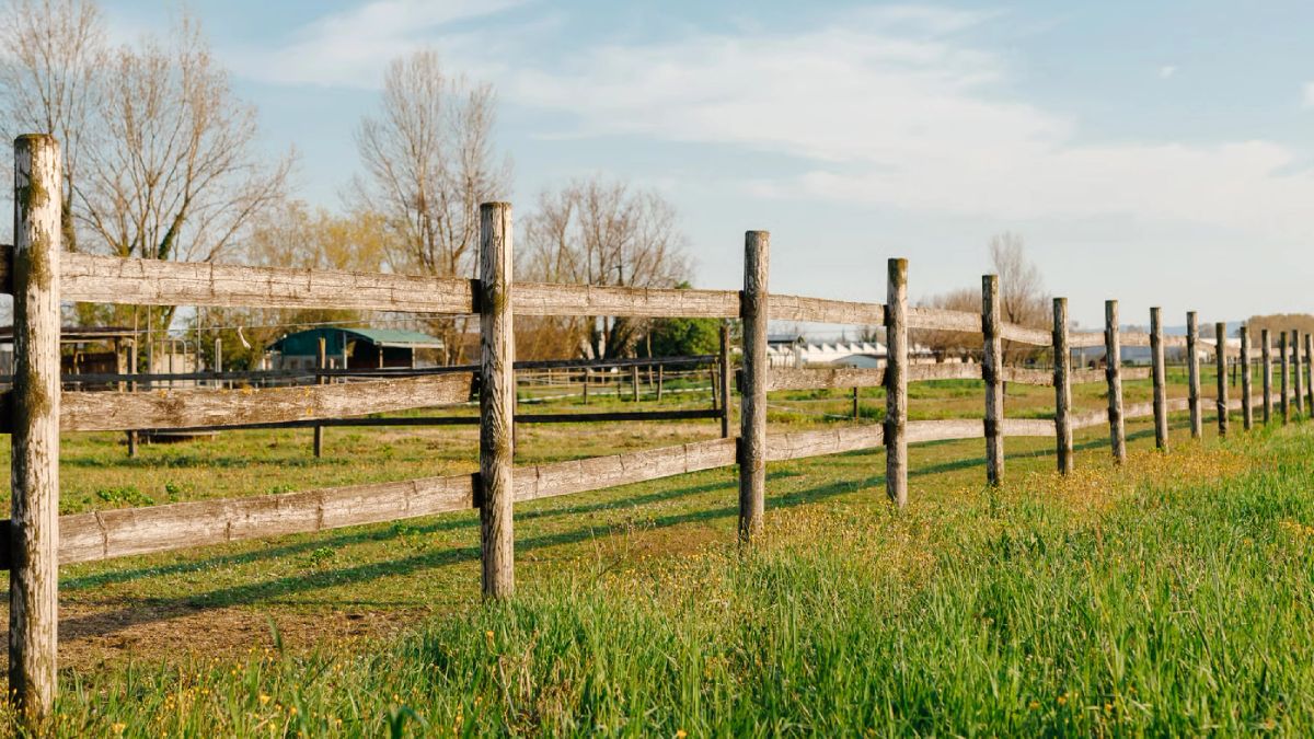 Terreno rural cercado con postes de madera y galpones agrícolas al fondo, en Chile