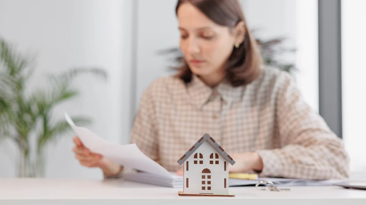Mujer revisando los documentos para vender su casa, con una maqueta de vivienda sobre la mesa