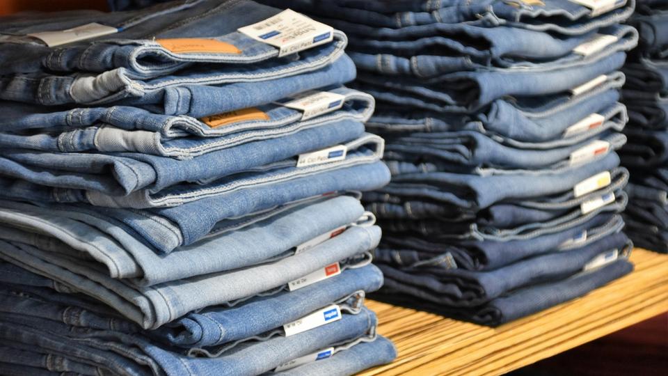Równe stosy poskładanych niebieskich spodni dżinsowych na drewnianym regale magazynowym, przygotowane do transportu odzieży lub sprzedaży detalicznej. Równe stosy poskładanych niebieskich spodni dżinsowych na drewnianym regale magazynowym, przygotowane do transportu odzieży lub sprzedaży detalicznej.