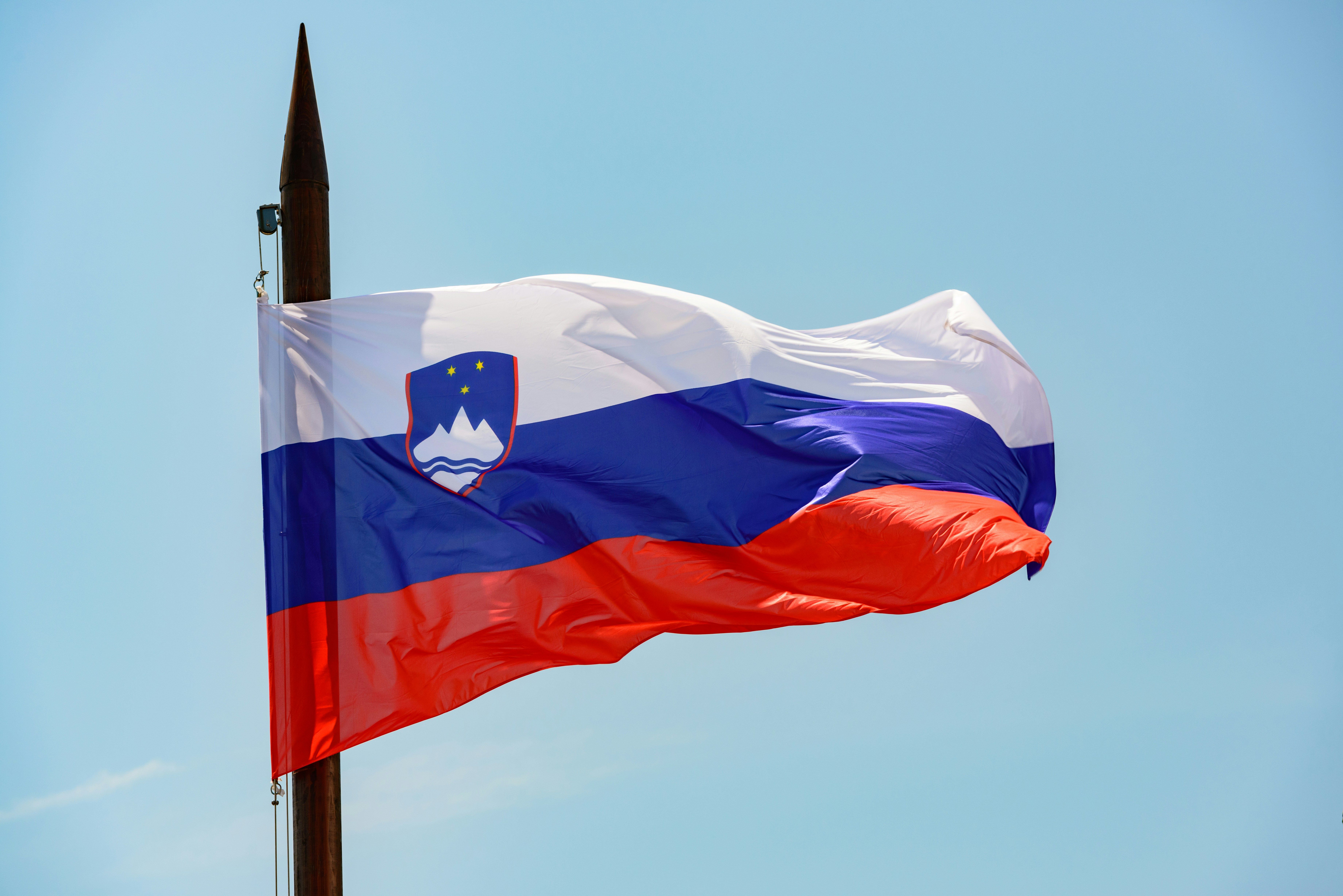 Flaga Słowenii powiewa na tle błękitnego nieba.