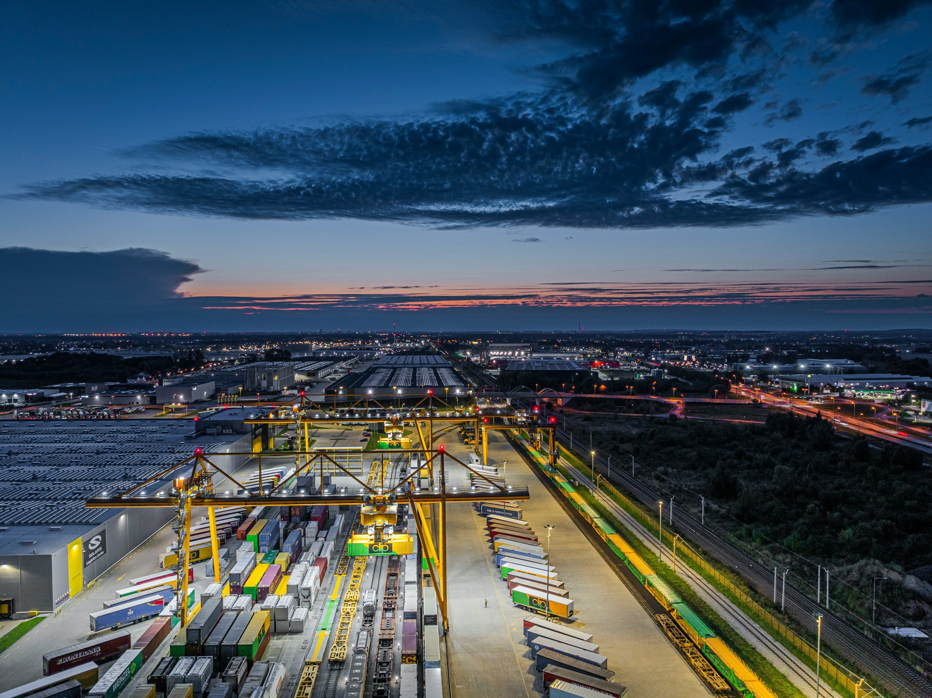 Terminal przeładunkowy i centrum logistyczne TSL z dźwigami bramowymi do cross-dockingu i przeładunku intermodalnego o zmierzchu.