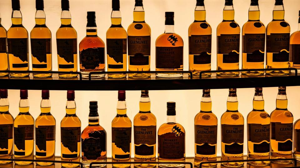 Podświetlone szklane półki wypełnione rzędami butelek whisky i ginu różnych marek w eleganckim barze. Idealne jako ilustracja asortymentu w logistyce napojów alkoholowych. Podświetlone szklane półki wypełnione rzędami butelek whisky i ginu różnych marek w eleganckim barze. Idealne jako ilustracja asortymentu w logistyce napojów alkoholowych.