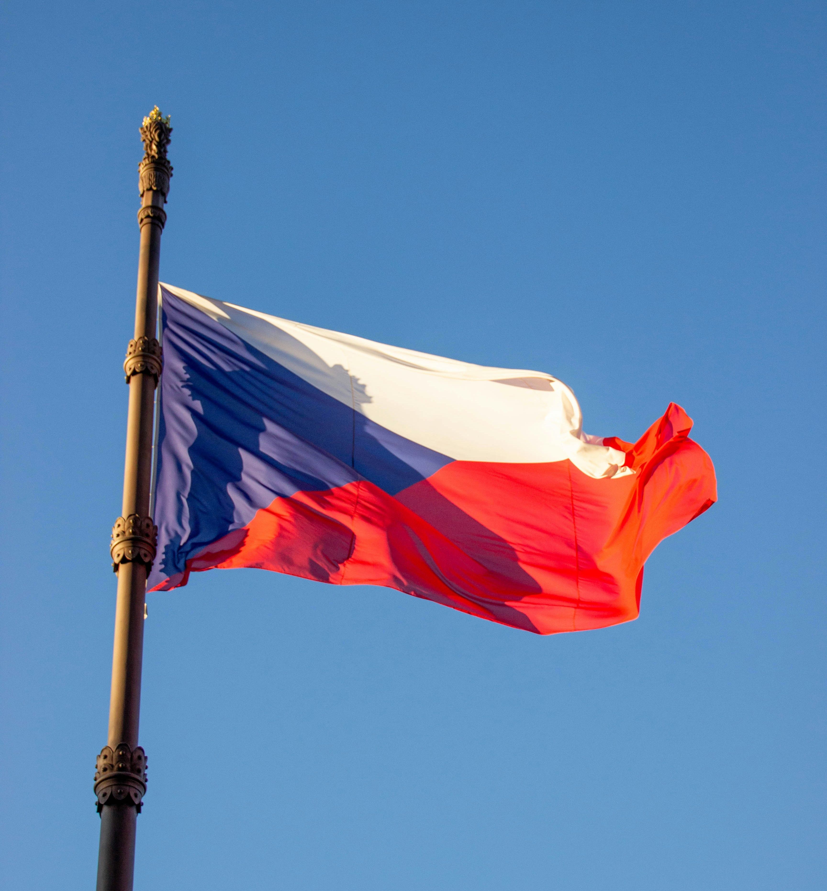 Flaga Czech powiewa na wietrze na tle bezchmurnego, błękitnego nieba.