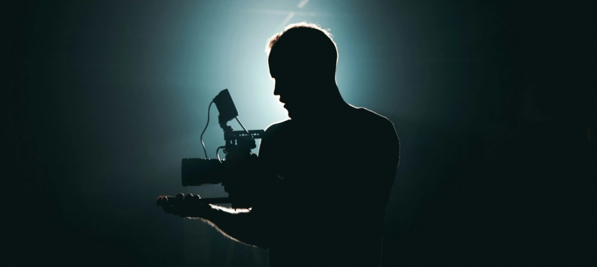 Man holding camera, spotlit from behind