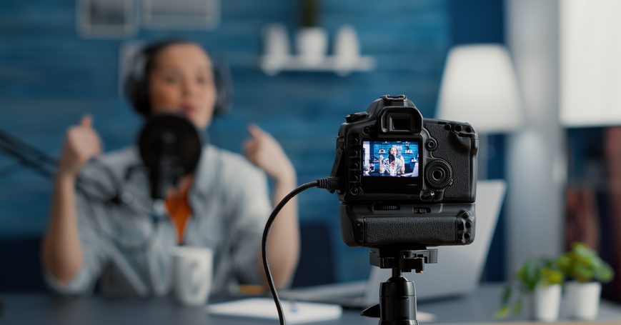 View of camera from behind in foreground, blurred in background shows the cameras view, someone wearing headphones speaking into a mic