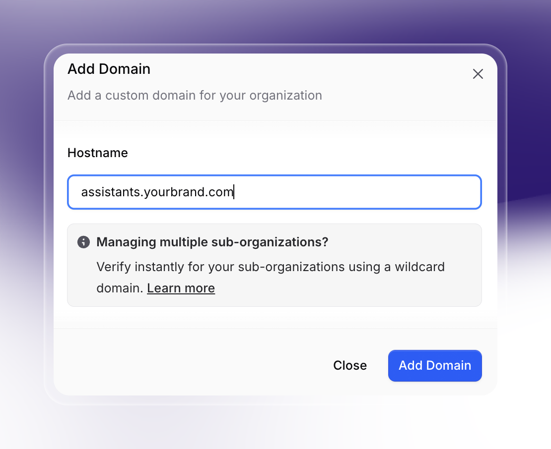 A pop-up dialog titled "Add Domain" for adding a custom domain to your organization in Invent. The sample domain “assistants.yourbrand.com” is entered, and there's guidance for verifying multiple sub-organizations with wildcard domains.