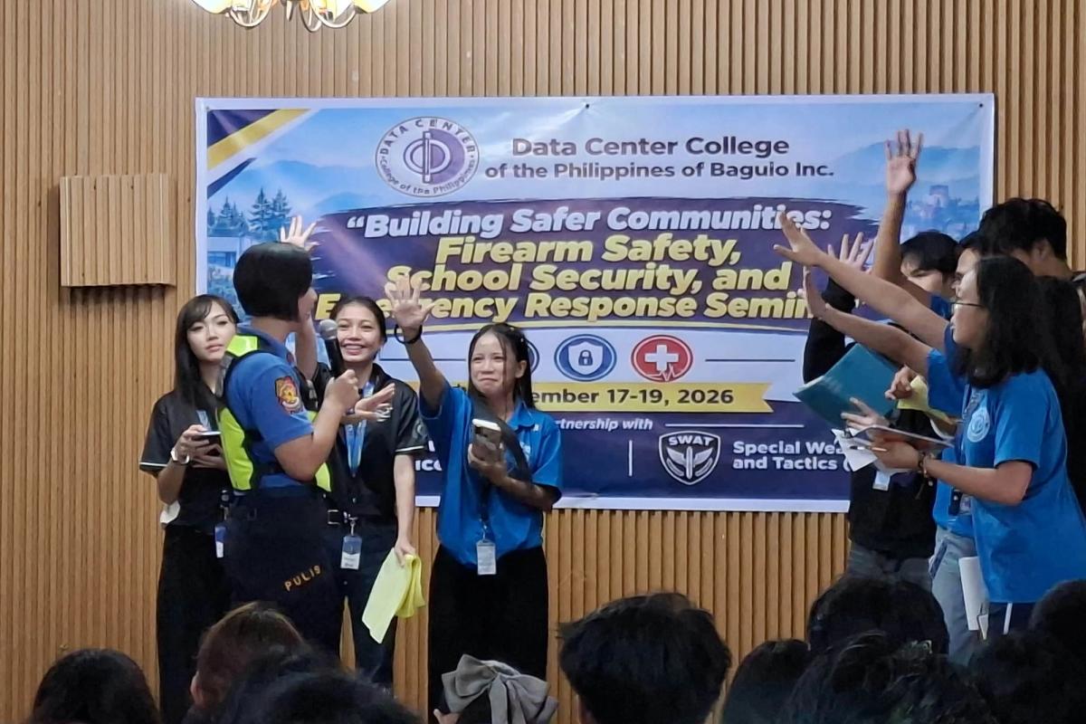 Students and officials raising their hands on stage in front of the Building Safer Communities seminar banner