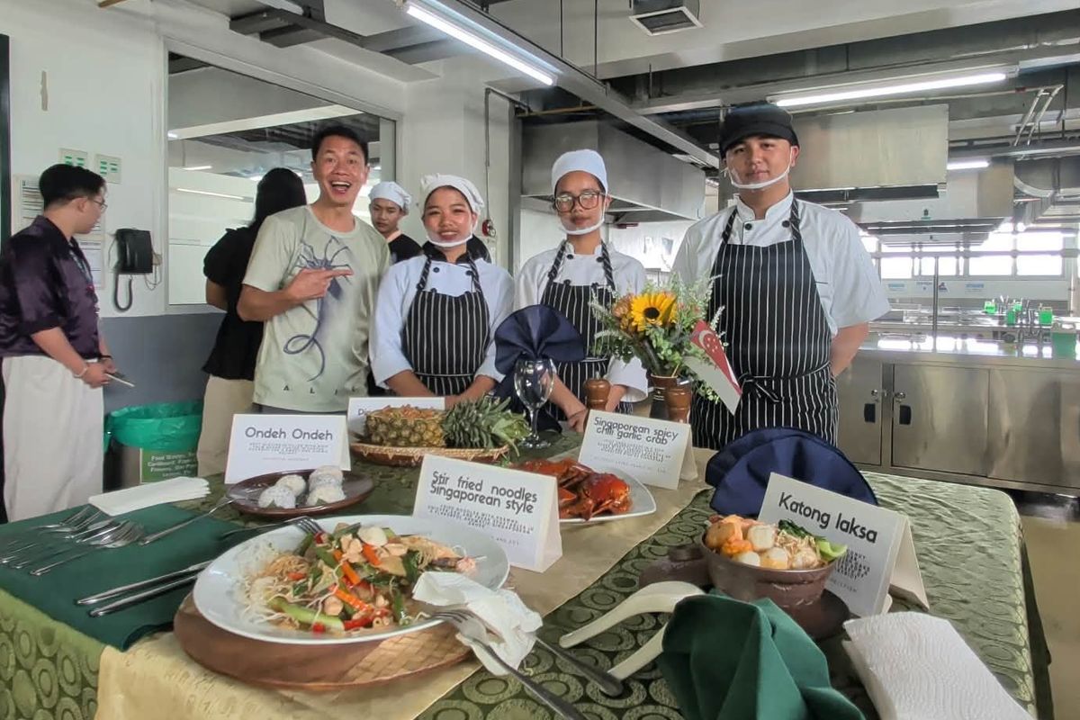 DCCP culinary students in chef uniforms stand behind a buffet table of Singaporean dishes including stir-fried noodles, chili crab, Katong laksa, and ondeh ondeh.