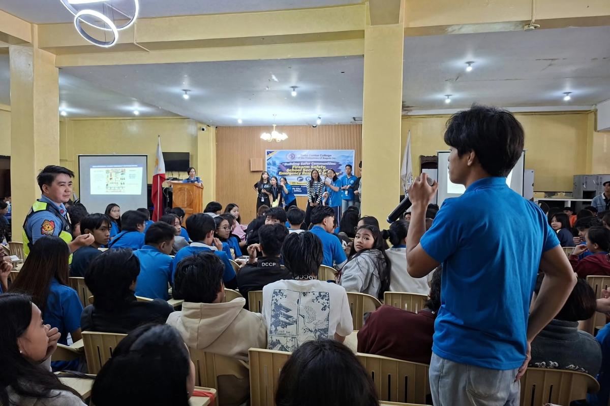 Student in a blue uniform speaking into a microphone while addressing fellow students seated in the seminar hall