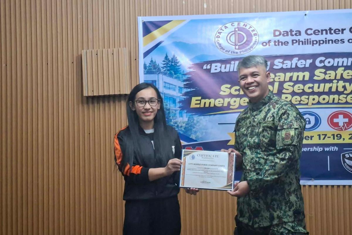 DCCP representative presenting a certificate of appreciation to a uniformed speaker in camouflage in front of the seminar banner