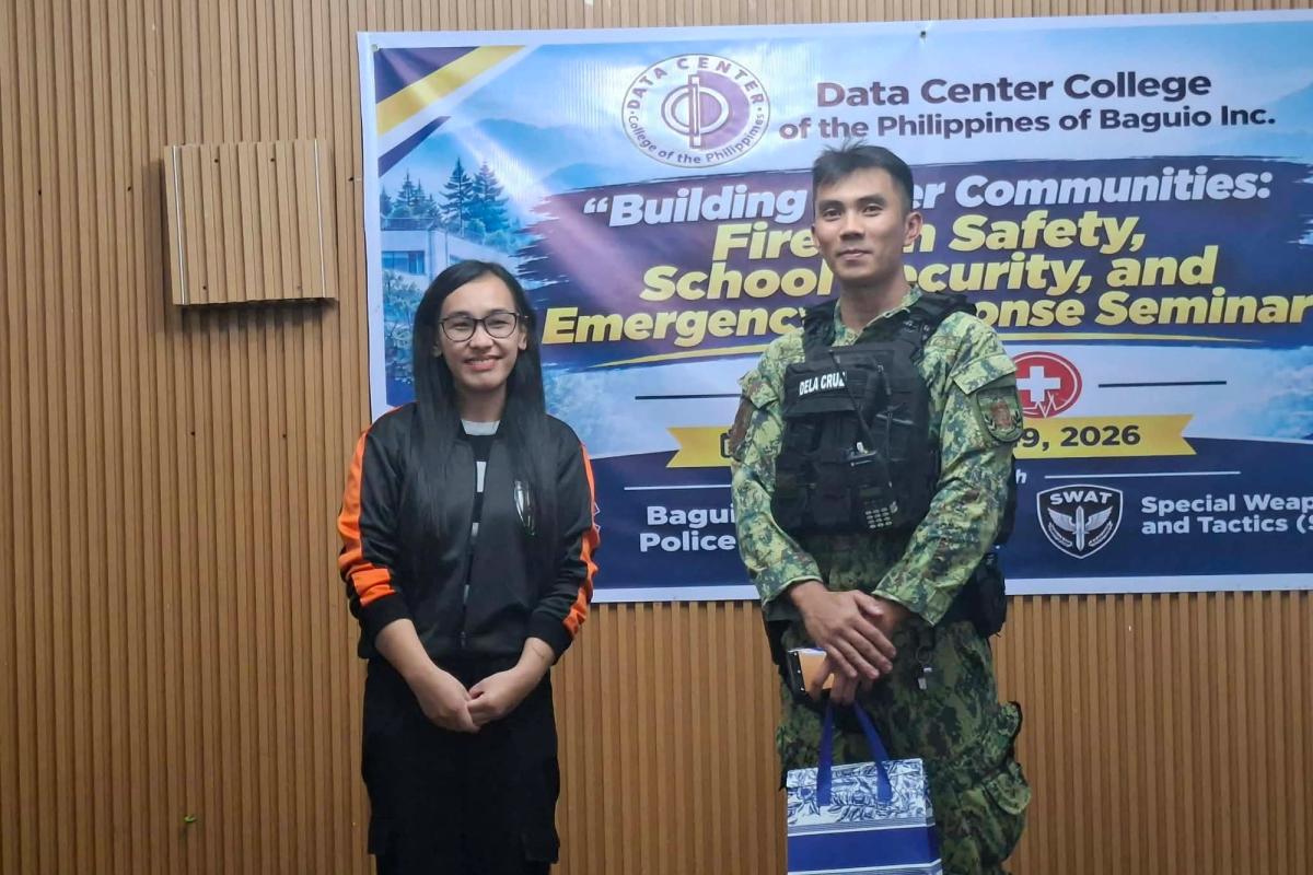 DCCP representative standing with a police officer in camouflage uniform in front of the Building Safer Communities seminar banner