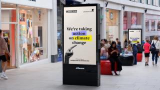 Digital advert in shopping centre reading 'We're taking action on climate change'