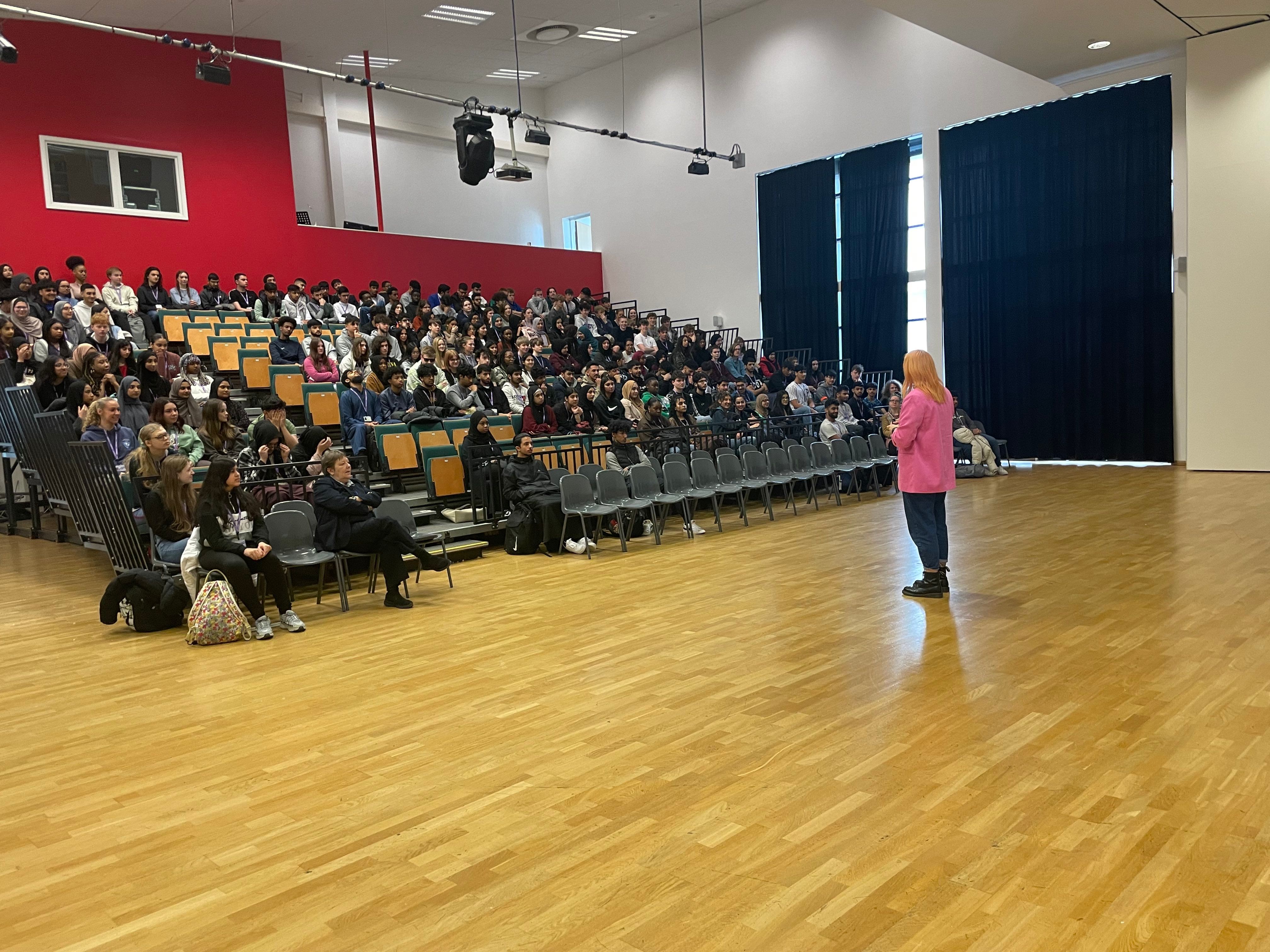 Woman in pink jacket standing in front of audience of high school students