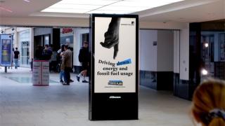 Digital advert in shopping centre reading 'Driving down energy and fossil fuel usage'