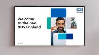 Screen on wall with text reading 'Welcome to the new NHS England' and an NHS England logo.