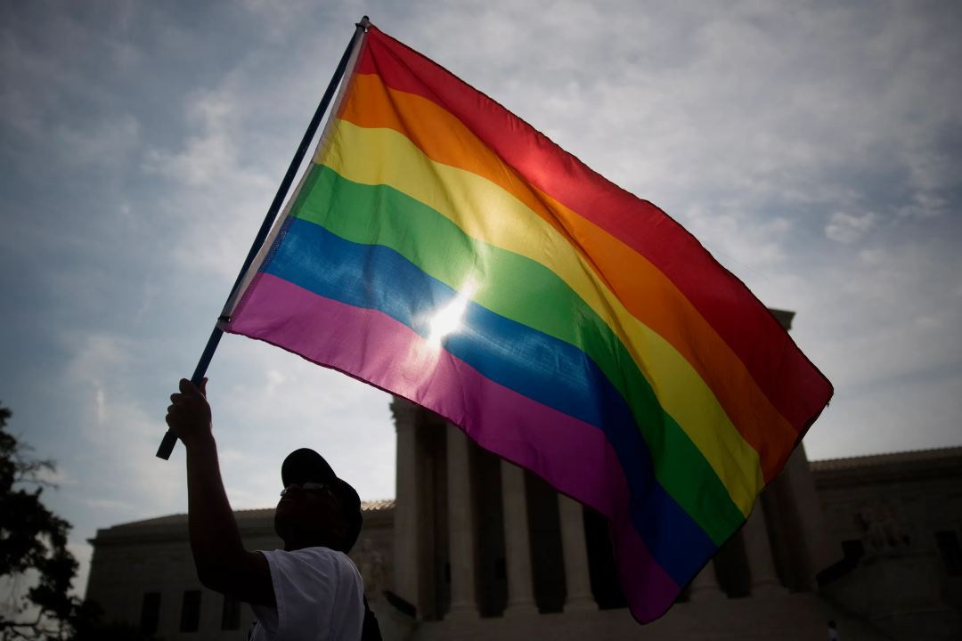 man holding a rainbow flag outside a public building