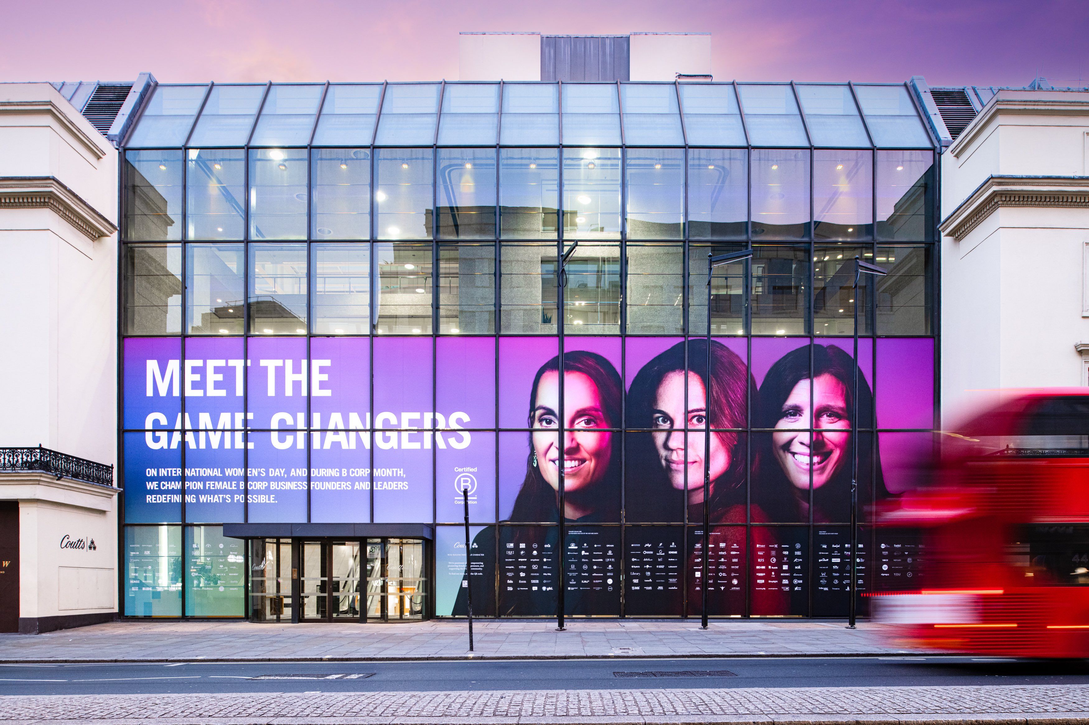 window of coutts bank with three women's faces on it, and lots of logos that are too small to see