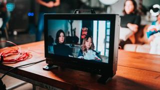 TV on desk shows image of women being filmed, they are sat on a sofa