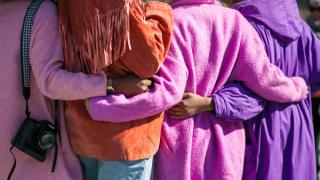 A group of four people from the back, each wearing a bright pink or purple jacket. They're hugging each other