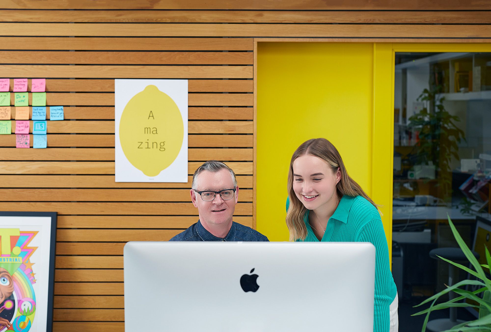 man in blue shirt and women in turquoise shirt looking at computer in front of a wooden background
