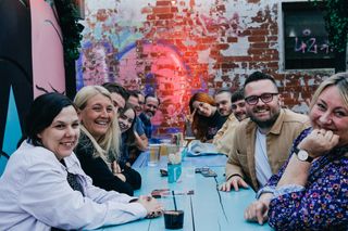 Group of people sat around table looking happy, with graffiti in background - they're at junkyard golf
