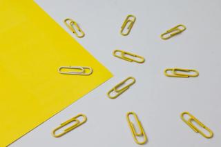 one white paperclip with multiple yellow paperclips