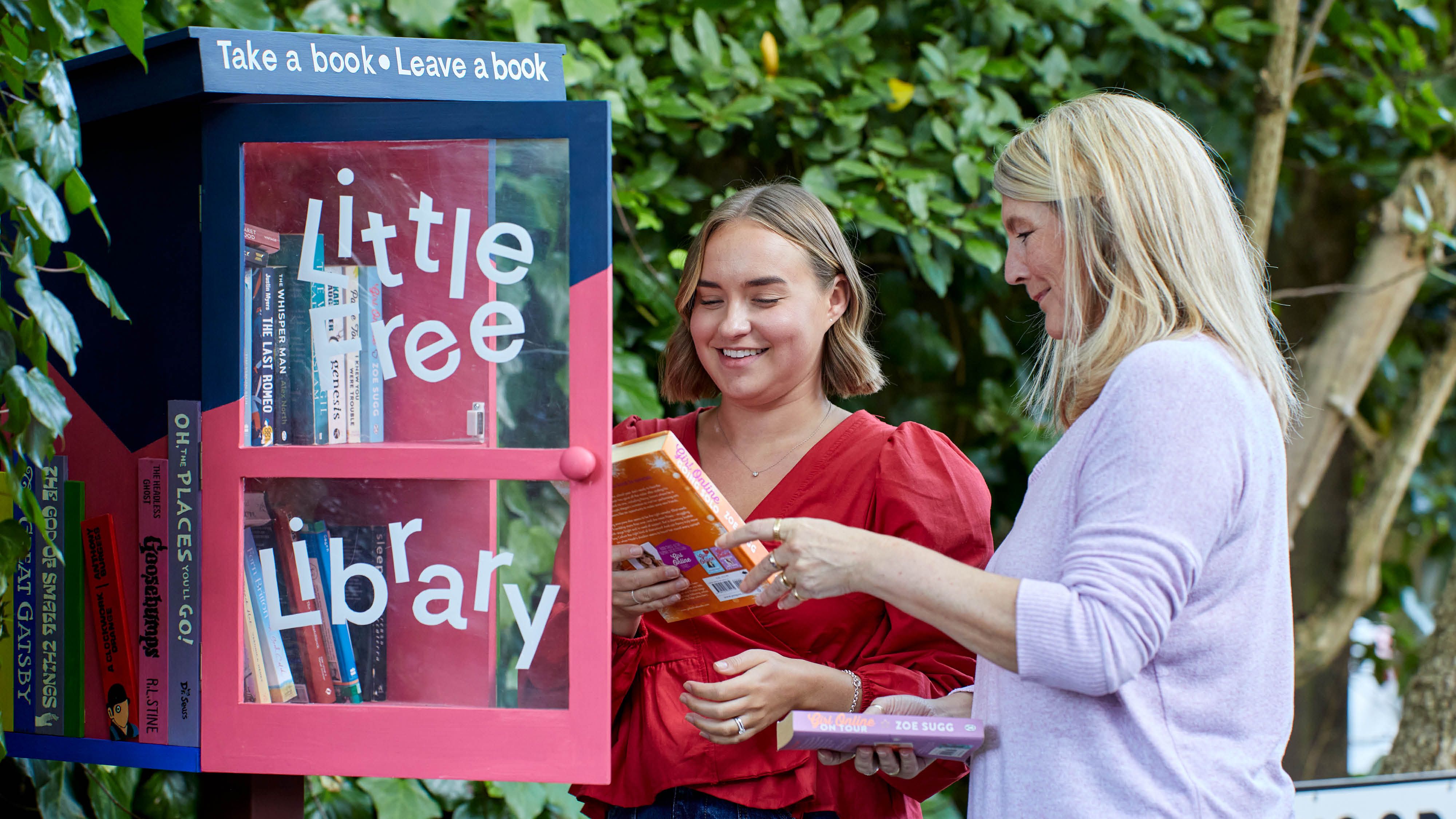 Two people putting books in a little library