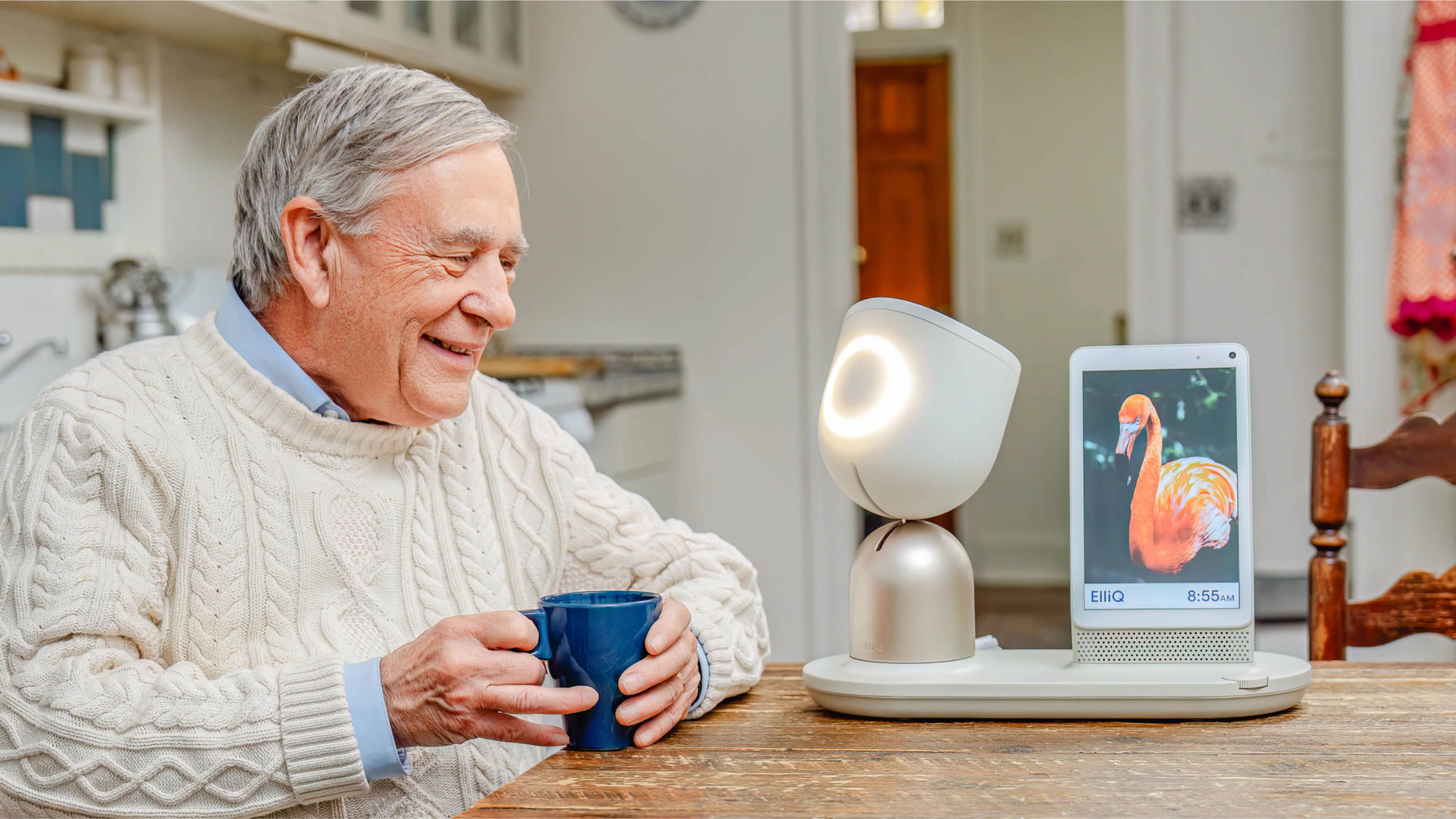 ElliQ on a table with an old person grinning at it