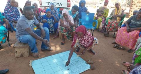 A woman marking a community mapping chart on the ground while residents observe