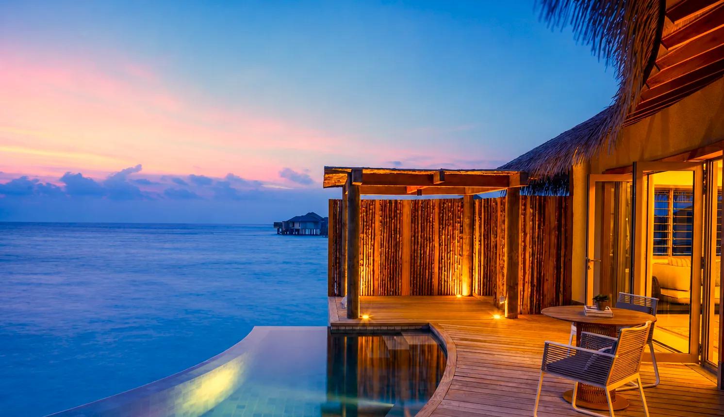 A Sunset Overwater Pool Villa's deck and pool lit at dusk, the lagoon turning gold