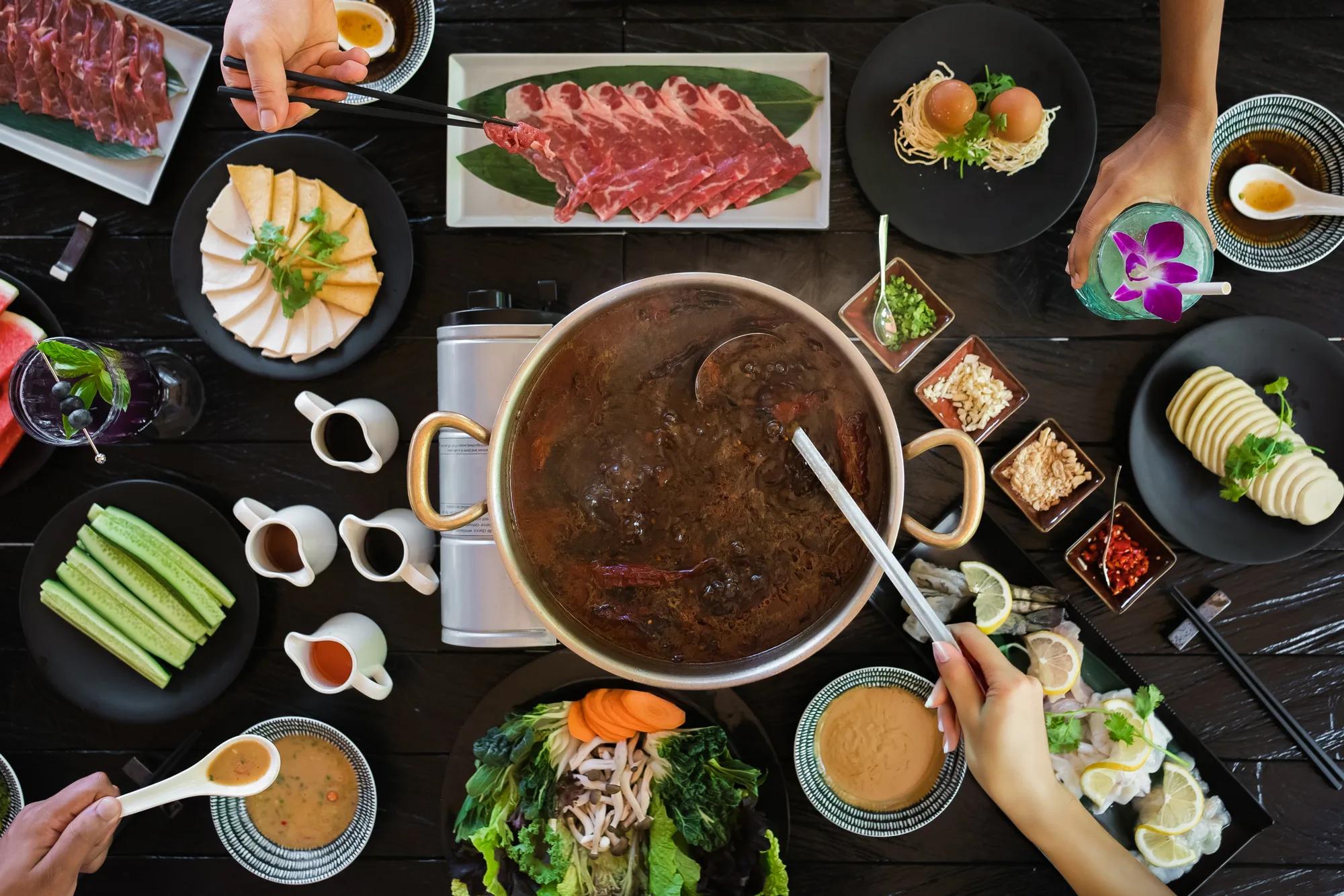 A shared hotpot spread at Vandhoo, JOALI's Asian restaurant, with sliced beef, tofu and condiment dishes laid around the pot