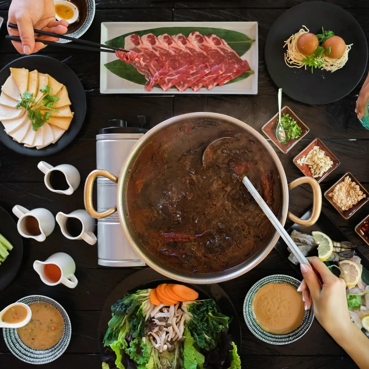 A shared hotpot spread at Vandhoo, JOALI's Asian restaurant, with sliced beef, tofu and condiment dishes laid around the pot